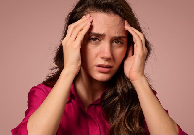 Frau fasst sich mit beiden Händen an die Schläfen | Migräneanfall